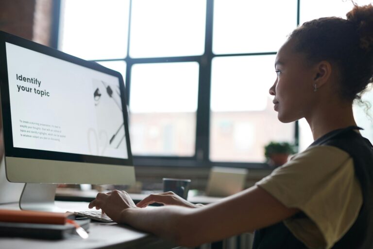 Girl looking at mac computer and on the screen of the mac computer the words "Identify your Topic pop up.